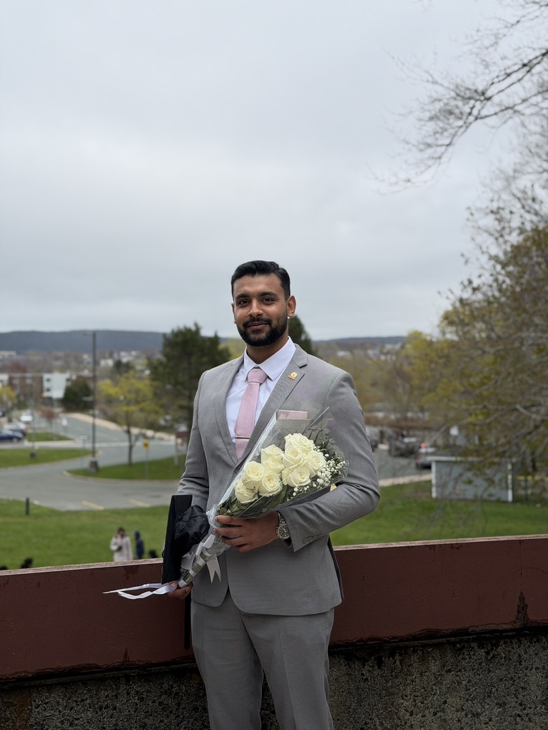 Adeel in a gray suit holding white flowers